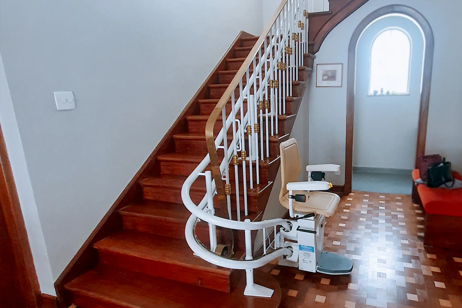 Treppenlift mit heller Kurvenschiene am Fuß einer Holztreppe im Wohnhaus