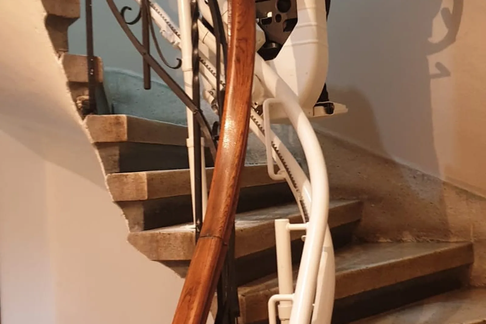 Treppenlift-Schiene entlang einer Steintreppe im Altbau, daneben ein historischer Handlauf aus Holz