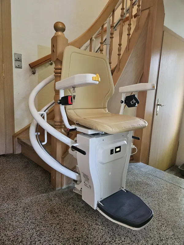 Kurvenlift-Referenz: Treppenlift mit beigem Polster in Parkposition am Fuß einer gewendelten Holztreppe
