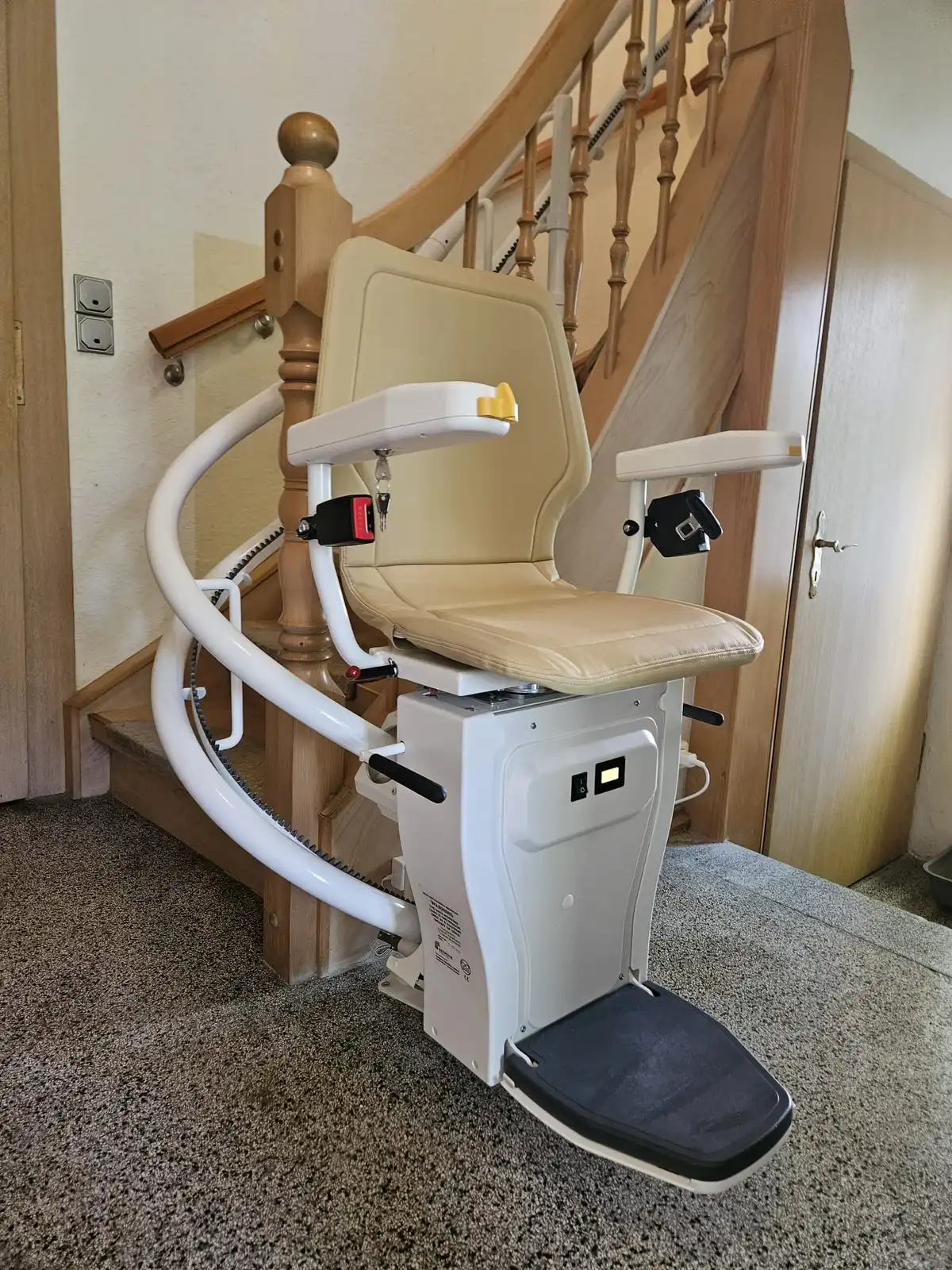 Kurvenlift-Referenz: Treppenlift mit beigem Polster in Parkposition am Fuß einer gewendelten Holztreppe